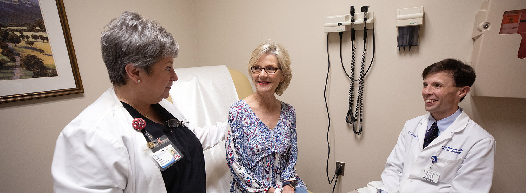 Two doctors talking to a patient in an exam room.